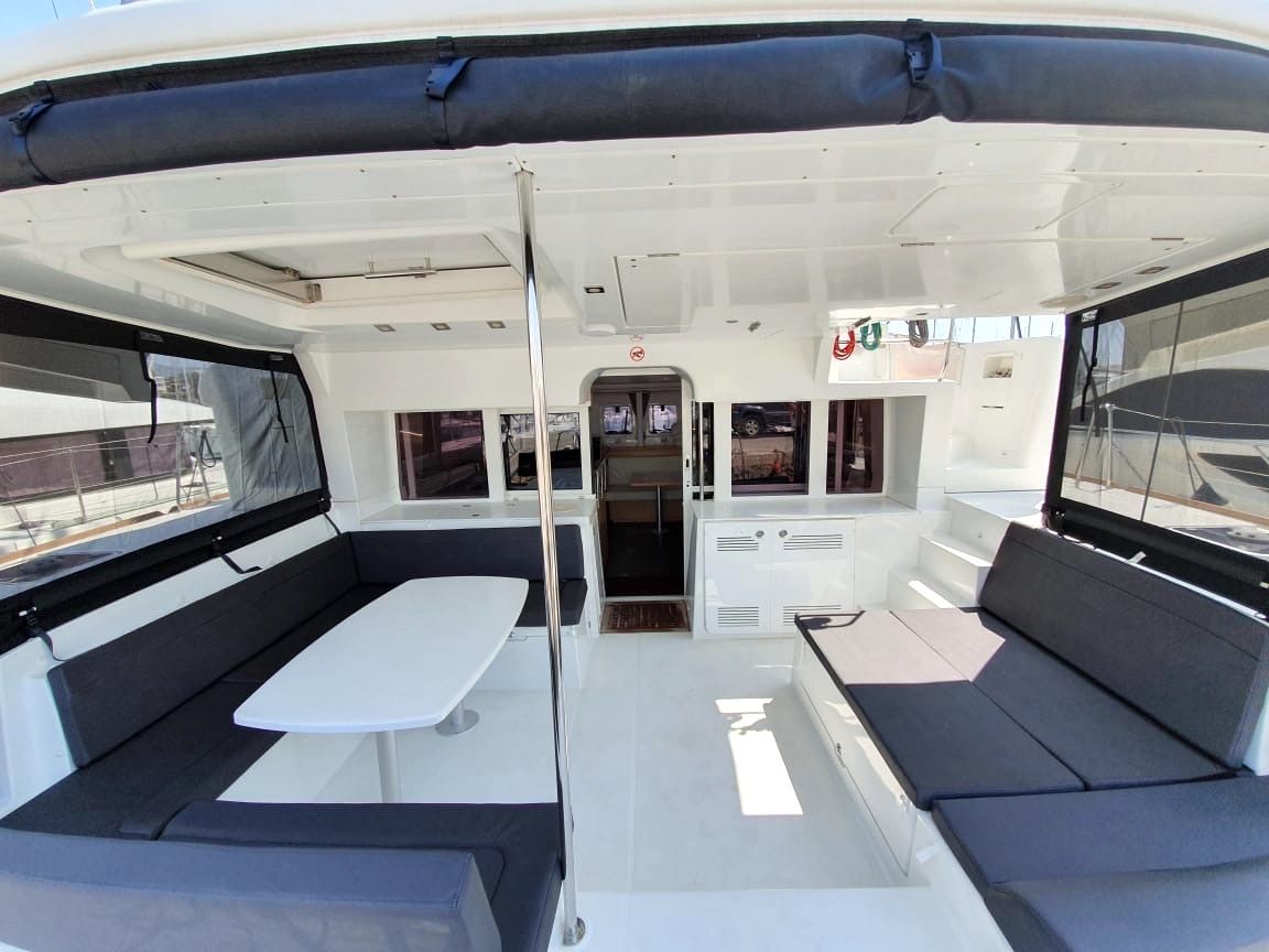 A boat interior with a central table, two seating areas, and a small enclosed space with a door.