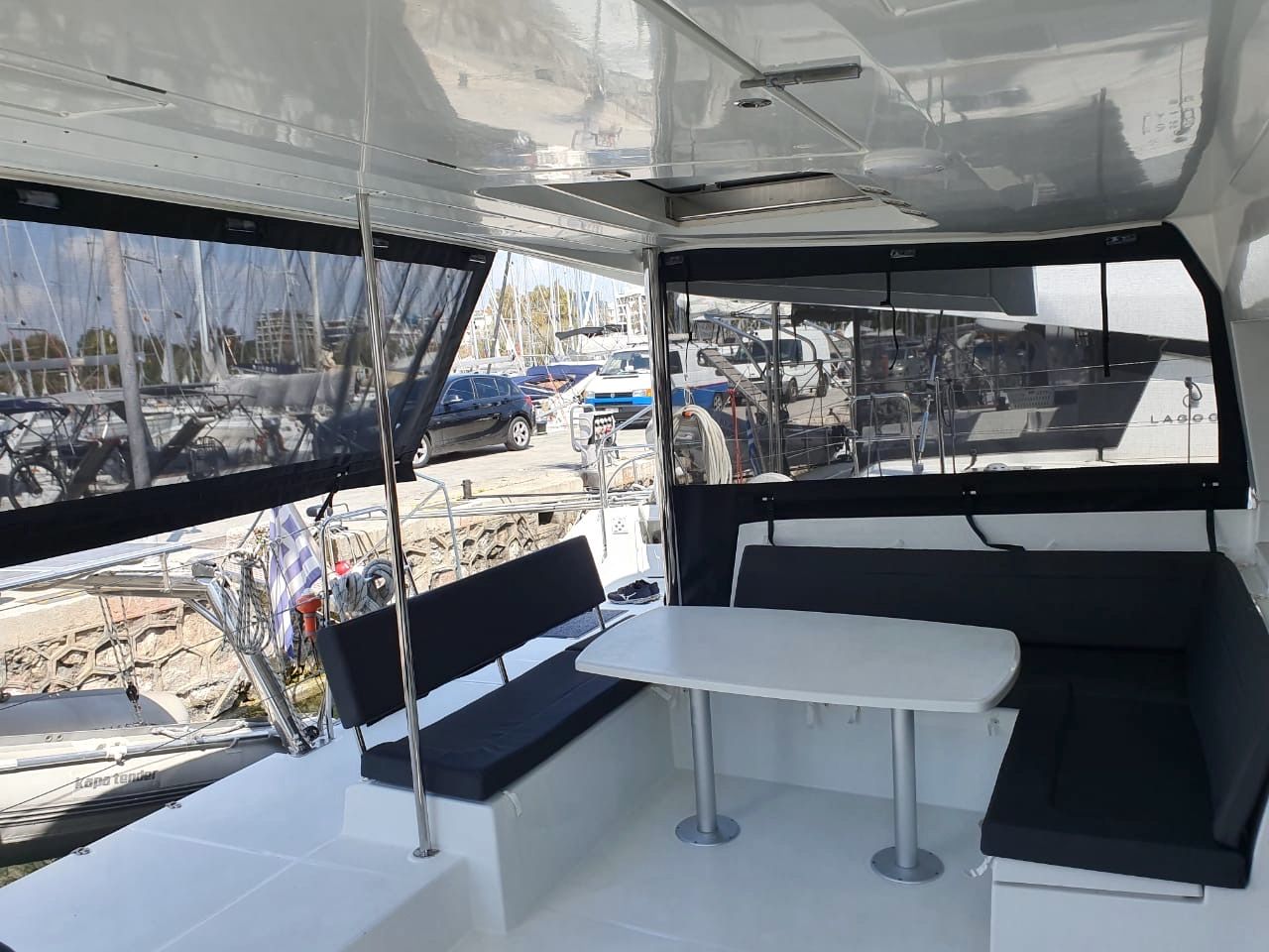 A boat's interior with a table and benches, a steering wheel, and a view of the marina.
