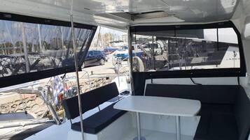 A boat's interior with a table and benches, a steering wheel, and a view of the marina.