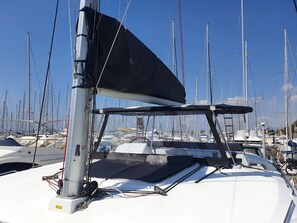 Eine Segelyacht mit abgedecktem Deck und mehreren Masten, vor Anker im Yachthafen, zusammen mit anderen Booten.