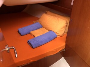 Ein kleines Bett mit einer orangefarbenen Matratze, zwei Kissen und zwei gefalteten Handtüchern.