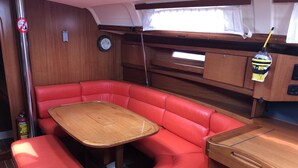 A compact RV interior with a red cushioned seating area, a wooden table, and a small kitchenette. - Sun-Kissed Sailing Adventure in the Majestic Islas Baleares (Sant Antoni de Portmany)
