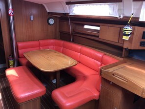 A compact RV interior with a red cushioned seating area, a wooden table, and a small kitchenette.