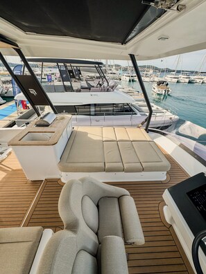 A yacht deck with seating, a control station, and a view of the marina.