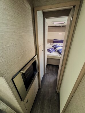 Ein schmaler Korridor führt zu einem Stockbett mit Kopfteil sowie einer kleinen Sitzecke mit einer Bank.