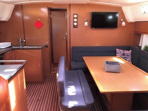 A compact interior with a kitchenette, a seating area with a table, a television mounted on the wall, and a door. - Sun-Kissed Sailing Adventure in the Ionian Islands, Lefkada (Lefkada)
