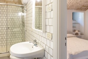Ein Badezimmer mit einem weißen Waschbecken, einer Duschkabine aus Glas und einer weiß gefliesten Wand.