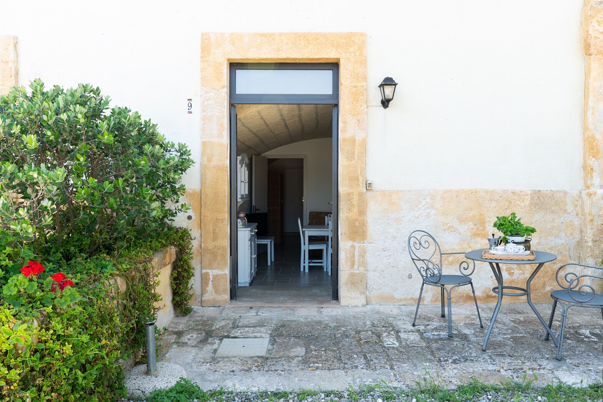 Une porte qui donne sur une pièce contenant une table et des chaises, une plante en pot et un luminaire fixé au mur.
