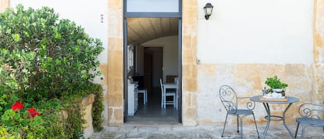 Una puerta que da a una habitación con una mesa, sillas, una planta en maceta y una lámpara fijada a la pared.