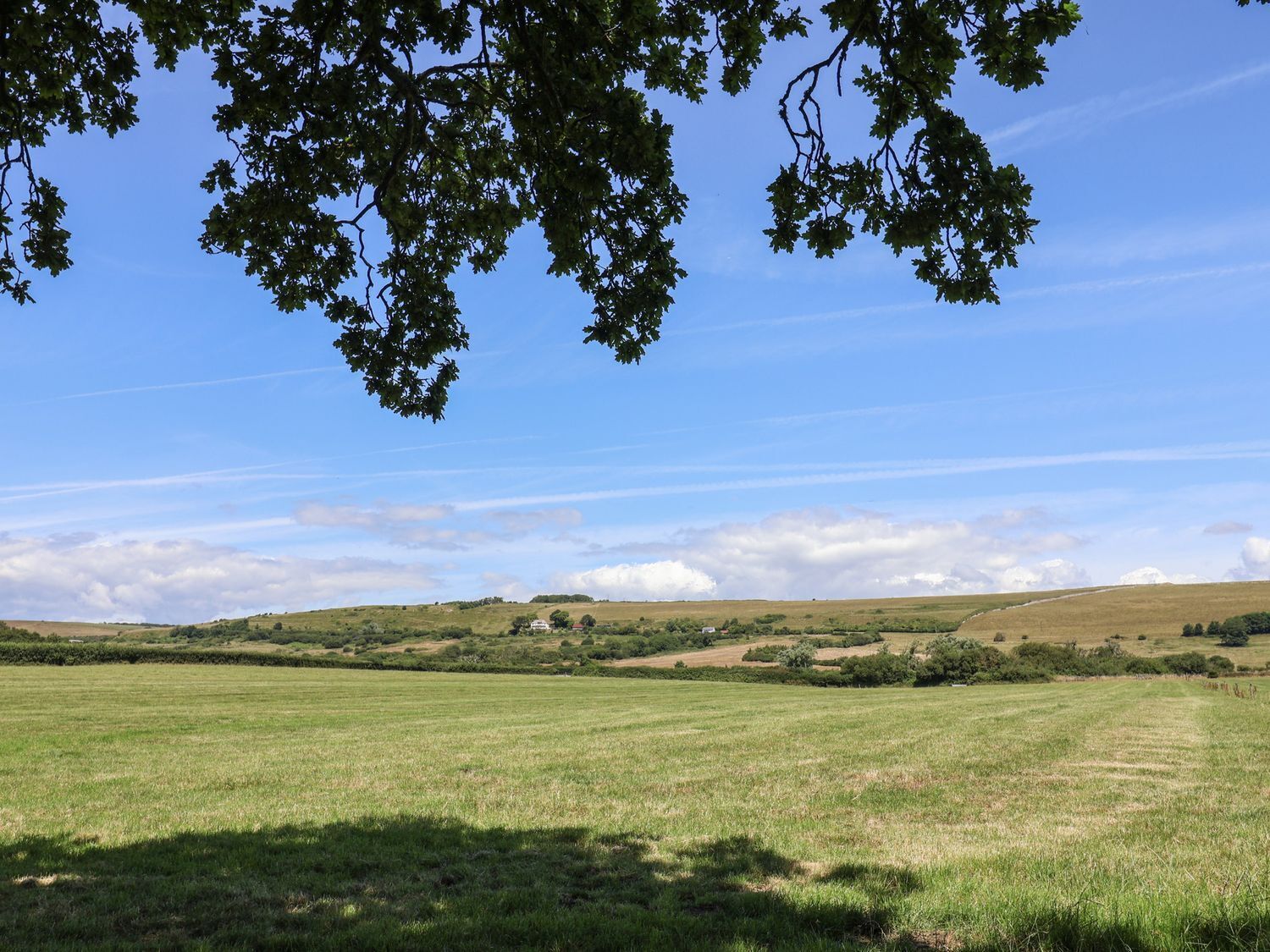 A rural landscape with a clear sky, rolling hills, and a field.