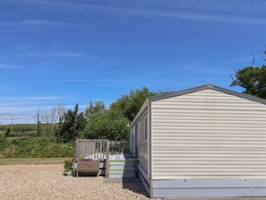 A single-story building with a sloped roof, a wooden deck, and a gravel driveway. - The Hideaway (Weymouth)