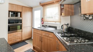 Una cocina compacta con armarios de madera, horno empotrado, cocina a gas y ventana con persianas.