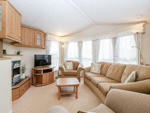 A living room with a TV, sofa, armchair, and wooden cabinets. - The Hideaway (Weymouth)