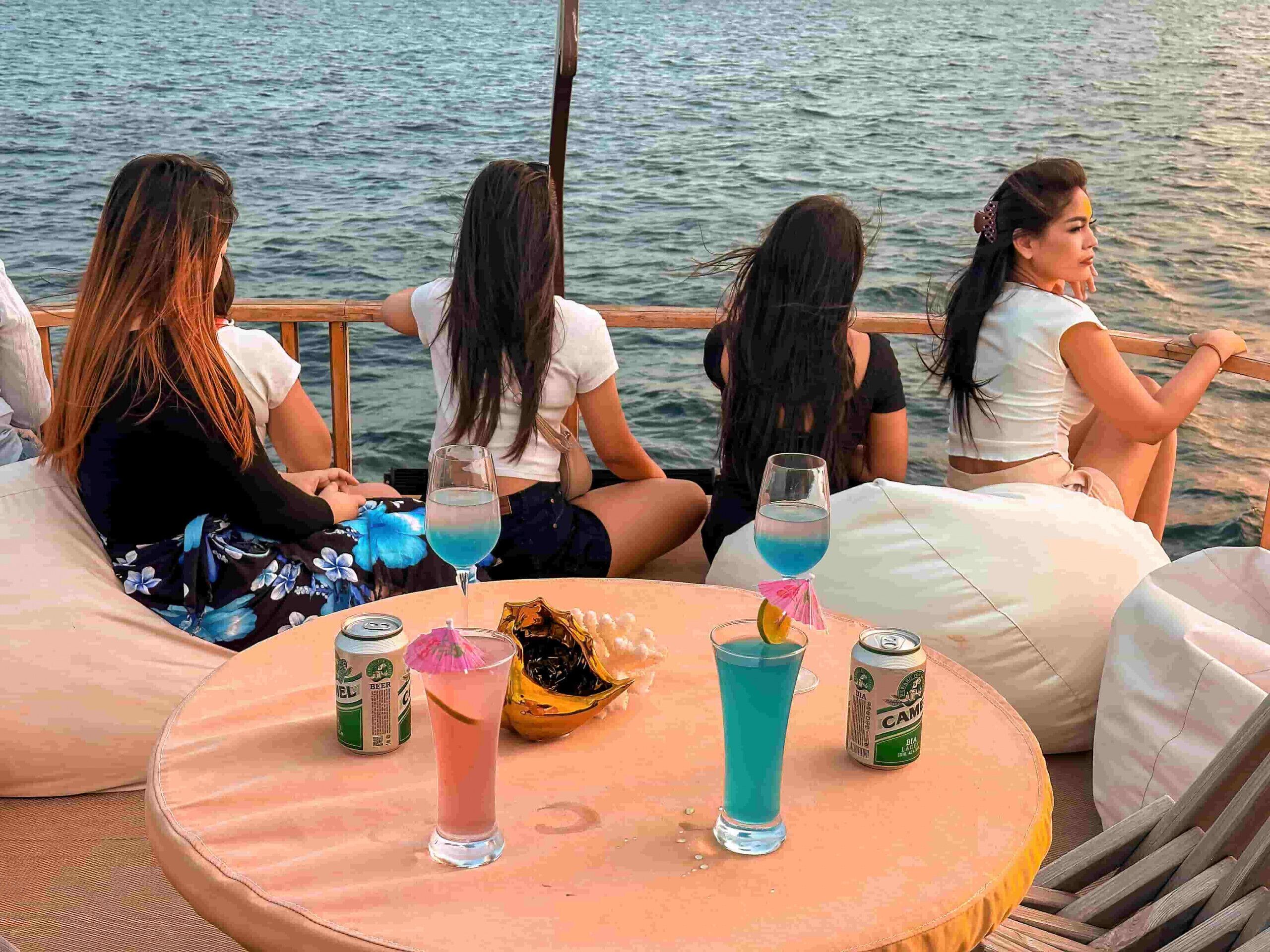 Un grupo de personas en un bote, con una mesa al frente donde hay bebidas y latas.