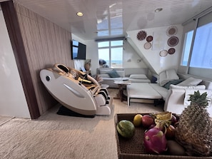 A modern living room with a massage chair, a sofa set, a small table, and a fruit basket.