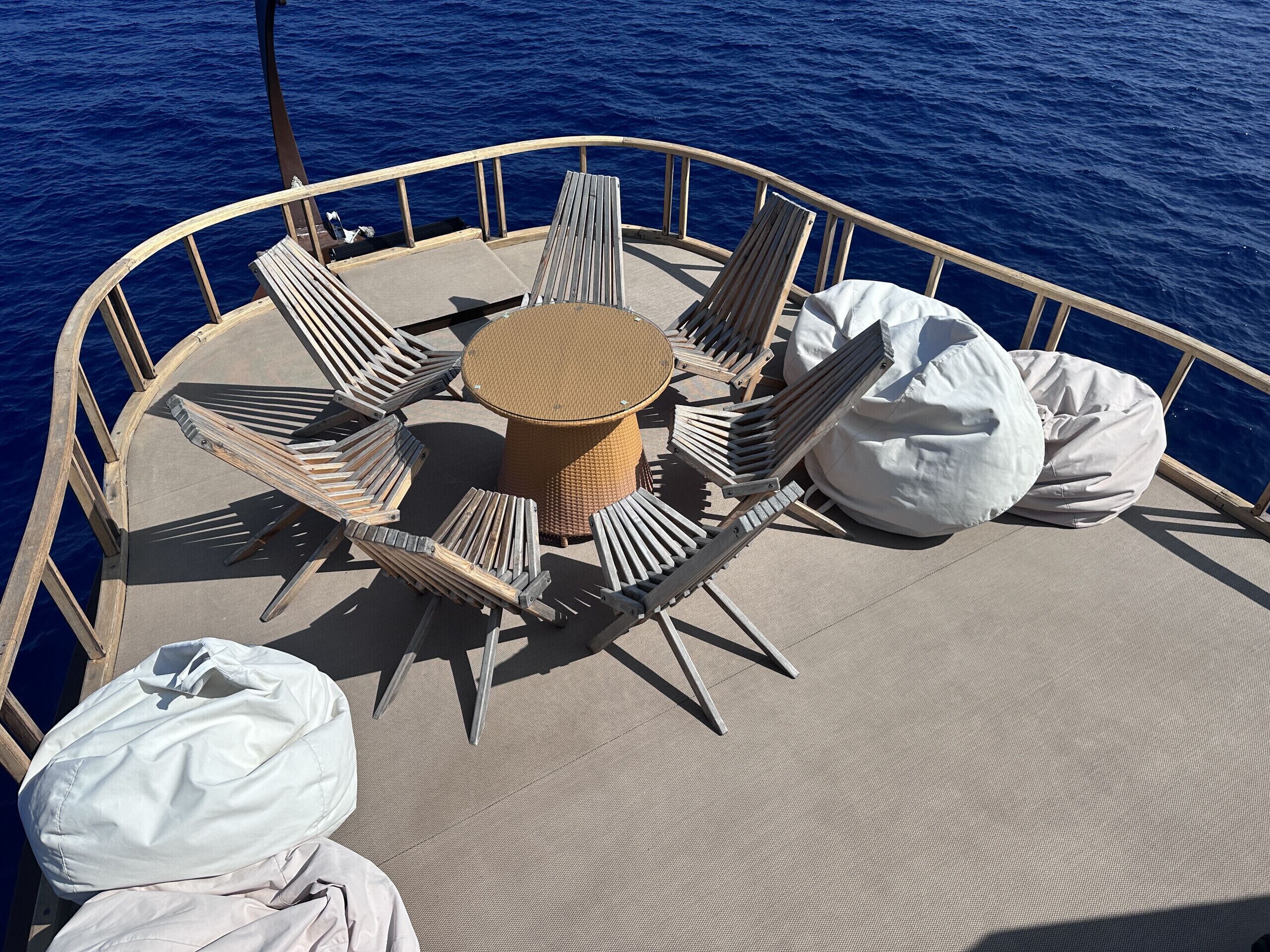 Une table ronde, entourée de chaises et de fauteuils en forme de sac de haricots, sur le pont d’un bateau.