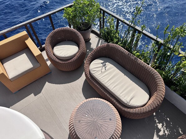 A deck with wicker furniture, including two chairs and a sofa, and a small round table.
