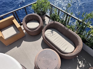 A deck with wicker furniture, including two chairs and a sofa, and a small round table.