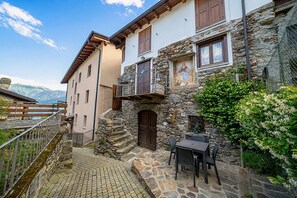 Un edificio de piedra con un balcón, una escalera y una mesa con sillas afuera.