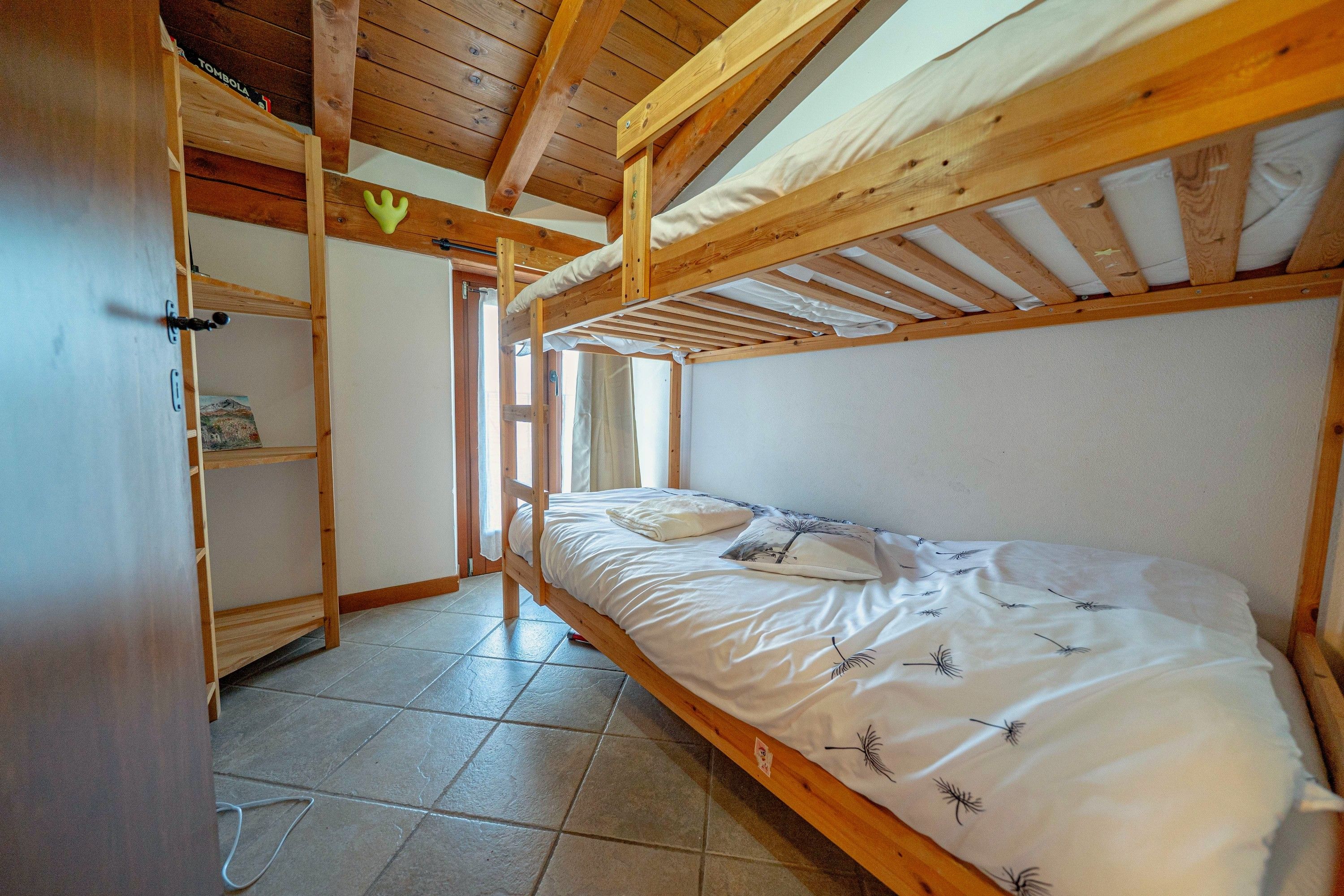A single-bed room with a wooden ceiling and a window.