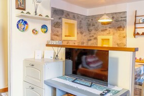 A room with a stone wall, a mounted television, a desk with a computer, and a shelf with decorative items.