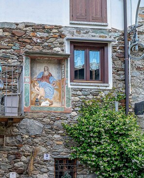 Un edificio de piedra con un mural, una ventana con persianas y una barandilla de metal.
