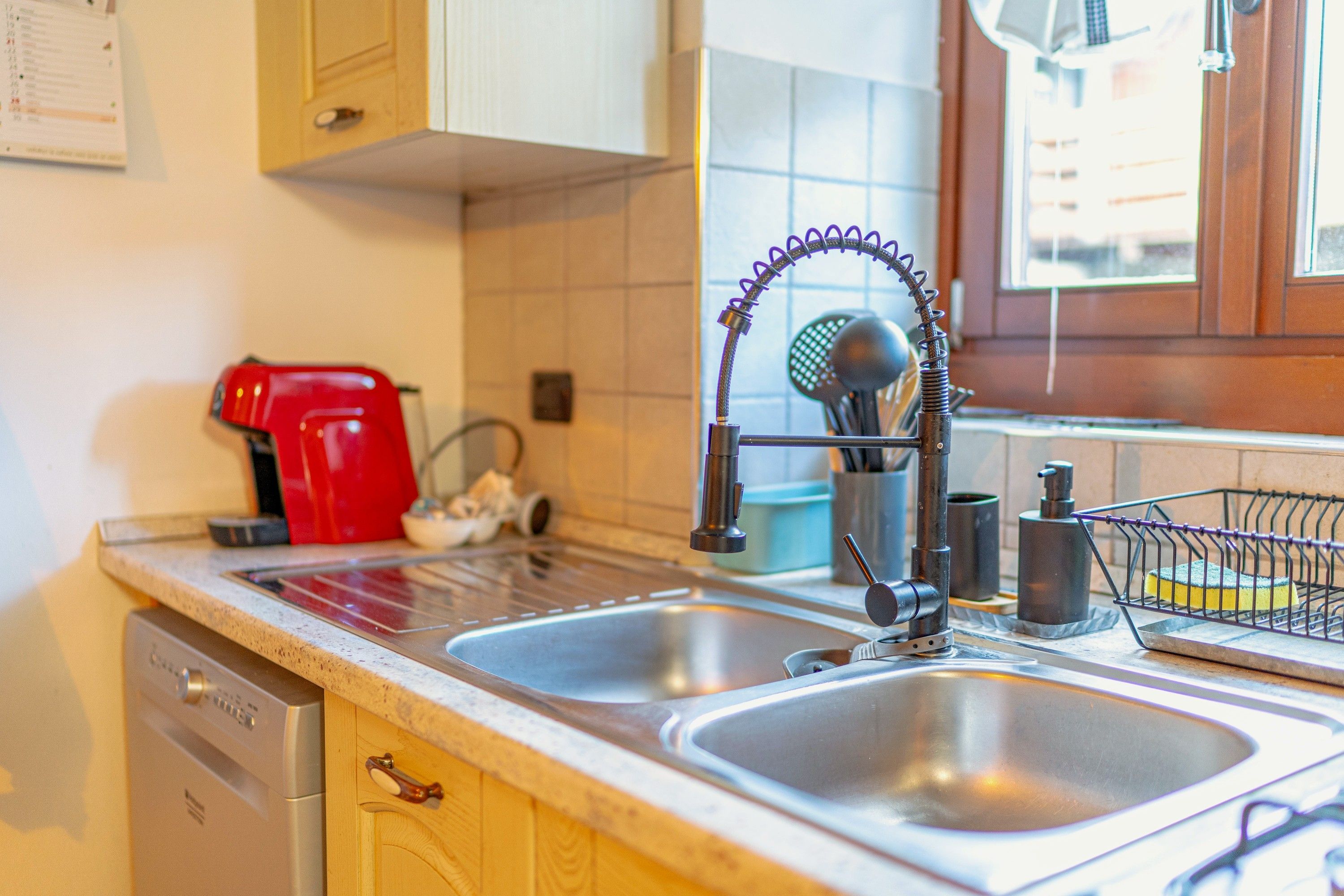Une cuisine équipée d’un évier à deux bacs, d’une cafetière rouge et d’un égouttoir à vaisselle.