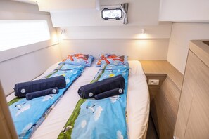 A small cabin with two beds, each with a blue sky-themed duvet and matching pillows. There is a small window with curtains and a light switch on the wall. - Sun-Kissed Sailing Adventure in Sibenik, Croatia (Primošten)