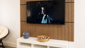 A modern living room with a flat-screen TV mounted on a wooden panel wall, a white entertainment unit with decorative items, and a light-colored wooden floor. - 2-Bedroom by beaches, airport, cruise hub,Wilton manors heart of Fort Lauderdale (Fort Lauderdale)