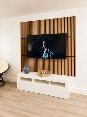 Ein modernes Wohnzimmer mit einem Flachbildfernseher an einer Wand aus Holzpaneelen, einer weißen Unterhaltungsanlage mit Dekorationselementen und einem hellen Holzboden.