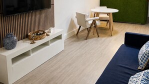 A modern living room with a flat-screen TV, a dining area with a white table and chairs, and a green wall with a plant. - 2-Bedroom by beaches, airport, cruise hub,Wilton manors heart of Fort Lauderdale (Fort Lauderdale)