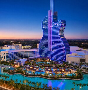 Ein Hotel mit einem gitarrenförmigen Gebäude, einem großen Schwimmbecken und einem Resortbereich mit mehreren Pools und Cabanas.