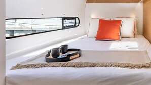 Une chambre moderne avec un puits de lumière, un lit agrémenté d’oreillers blancs et orange, une table de chevet avec un plateau, et une vue par la fenêtre.