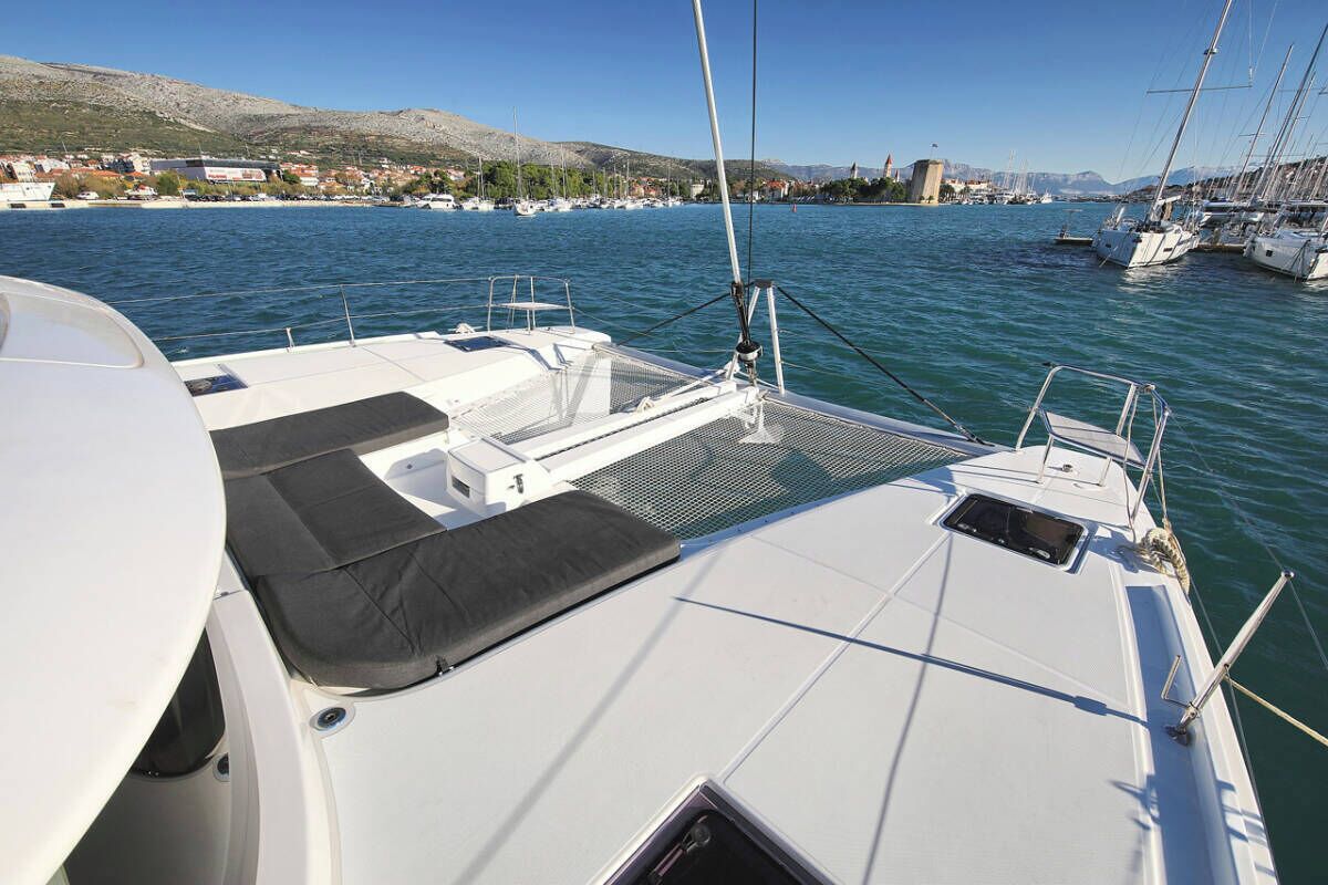 A boat's deck with a white hull, a black cushioned seating area, and a clear view of the marina and distant buildings.