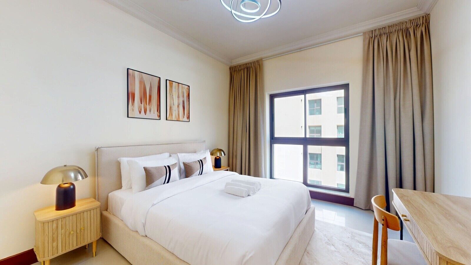 A hotel room with a bed, bedside tables, a desk, and a large window with curtains.