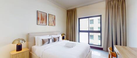 A hotel room with a bed, bedside tables, a desk, and a large window with curtains.
