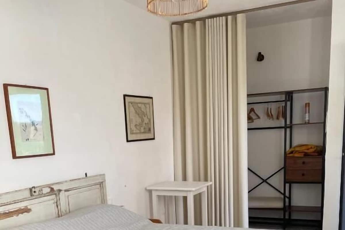Une chambre à coucher avec un lit, une petite table, une armoire et un rideau.