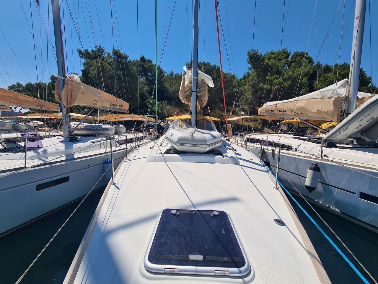 A marina with multiple sailboats docked, featuring a central walkway and a covered area with a canopy.