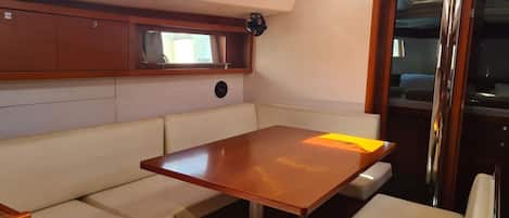 A cabin with a table and cushioned seating, a window, and a door leading to a galley.