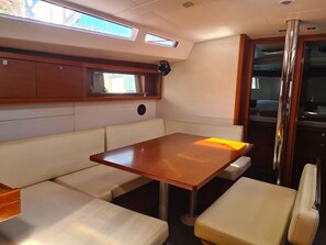 A cabin with a table and cushioned seating, a window, and a door leading to a galley.