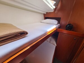 A bunk bed with a folded blanket, a small shelf with a fan, and a wooden cabinet.