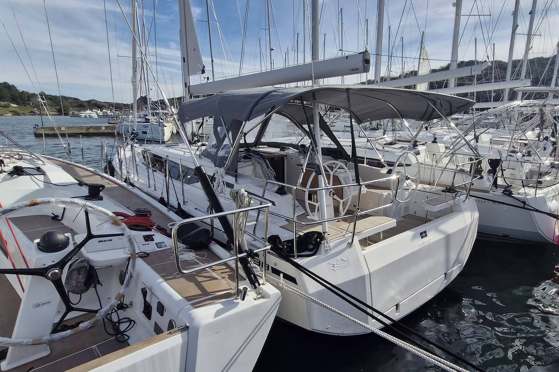 A marina with multiple sailboats docked, featuring a covered deck area and visible steering wheel.