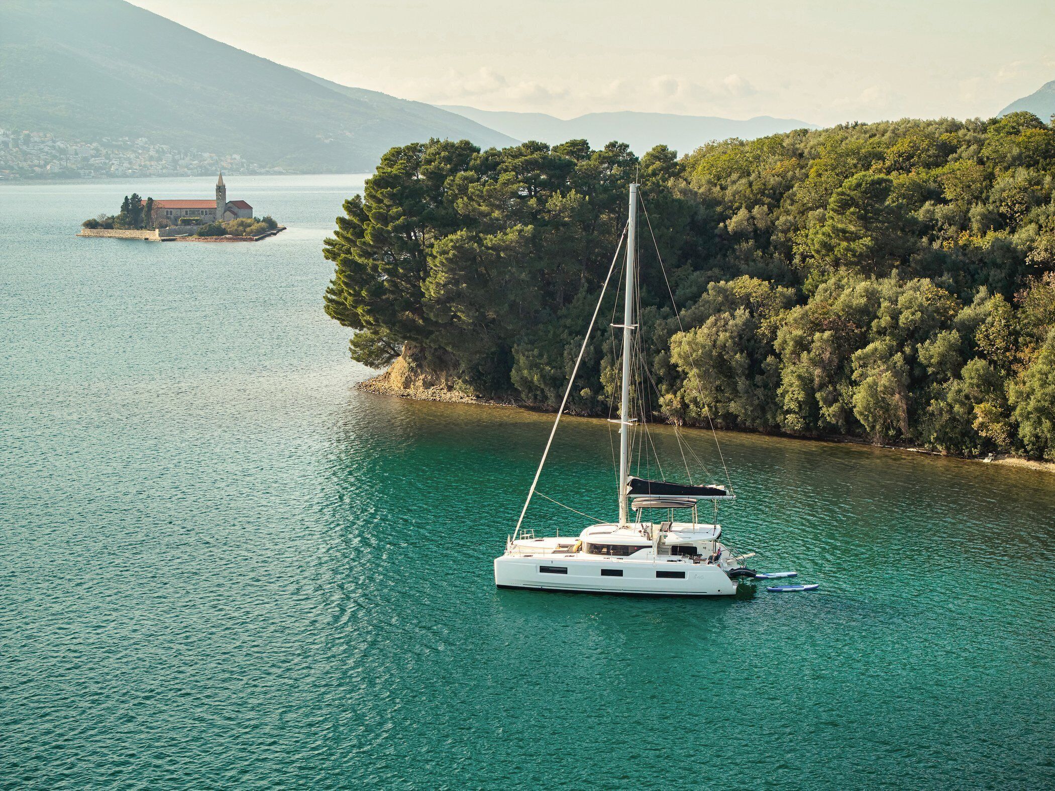 Ein Segelboot auf einem ruhigen See mit einer bewaldeten Insel im Hintergrund.