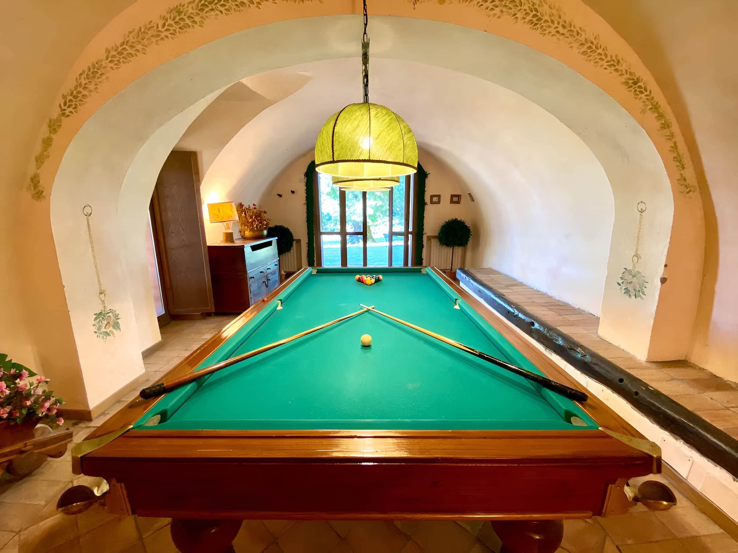 A pool table with a green felt surface, surrounded by a white wall with an arched doorway.