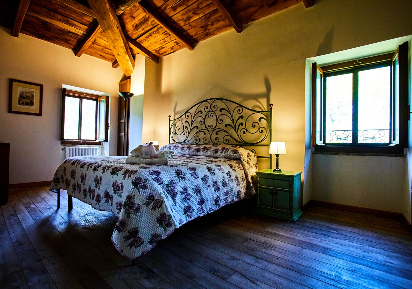 Una camera da letto con soffitto in legno, un letto con copripiumino floreale, un comodino con lampada e una finestra con vista.