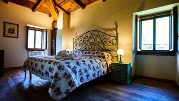 Una camera da letto con soffitto in legno, un letto con copripiumino floreale, un comodino con lampada e una finestra con vista.