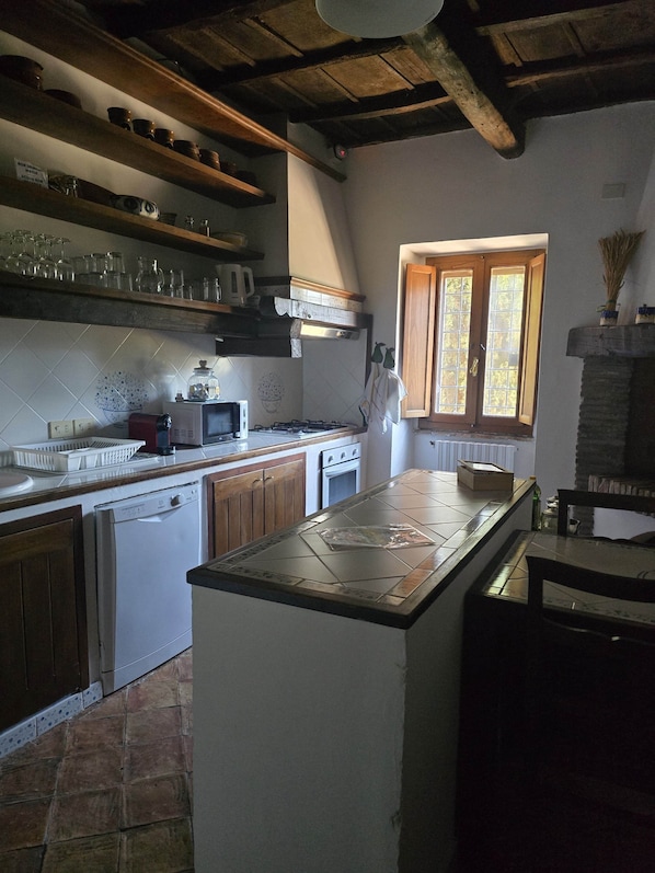 A kitchen with wooden cabinets, a tiled backsplash, a window with wooden shutters, and a stone fireplace.