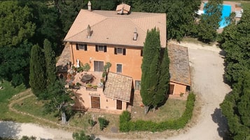 Una vista aerea di una casa a due piani con tetto in tegole, circondata da vegetazione e una piscina.