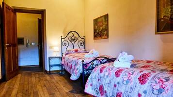 A bedroom with two beds, wooden flooring, a door, a nightstand, and a painting on the wall.