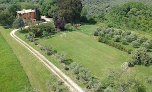 A large, open grassy field with a building and a goalpost, surrounded by trees and vegetation.